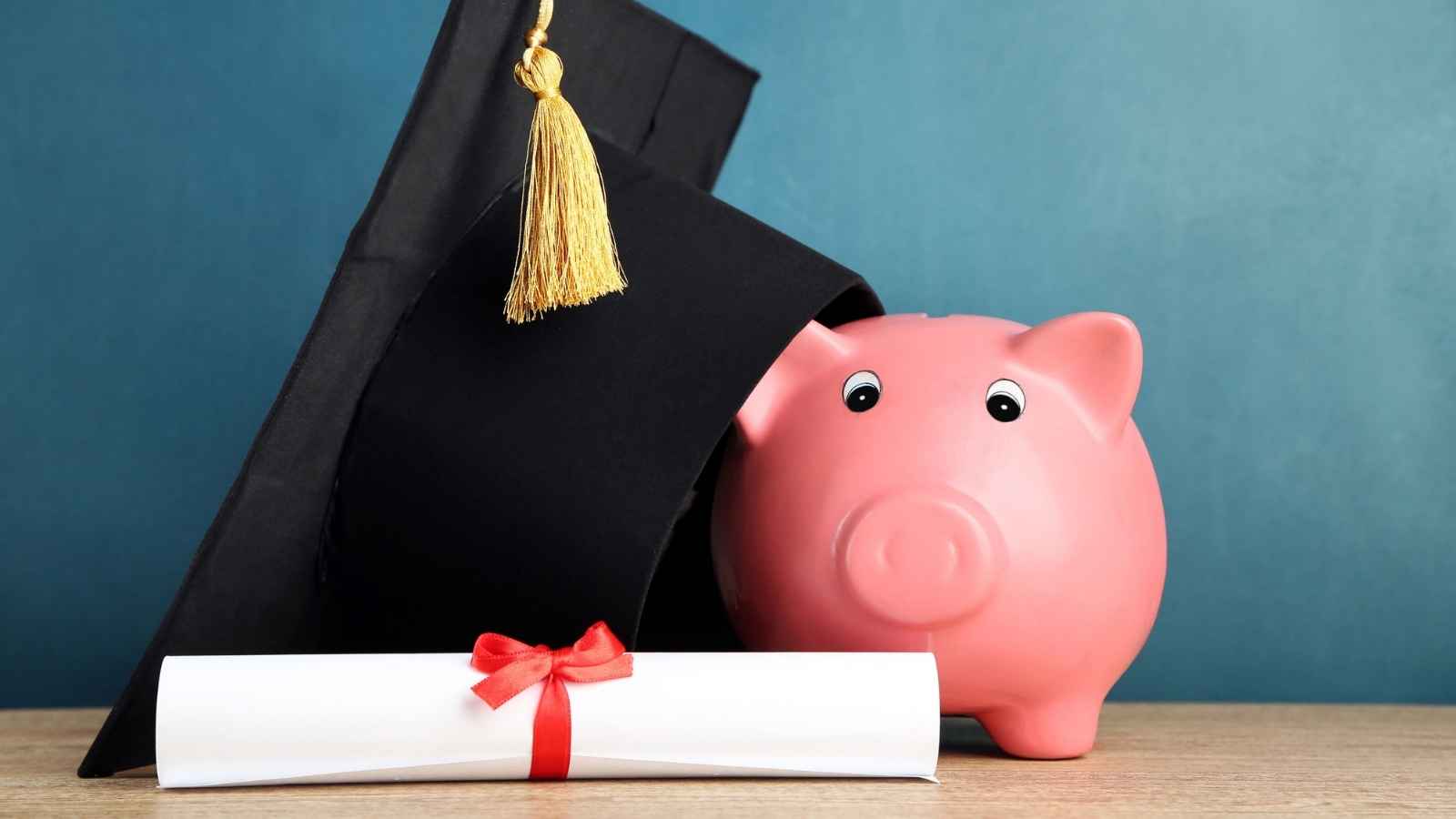 Piggy bank next to diploma and graduation cap