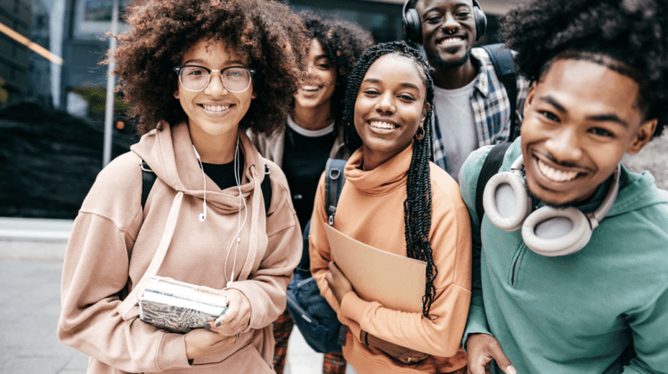 College students huddled close together holding books and smiling